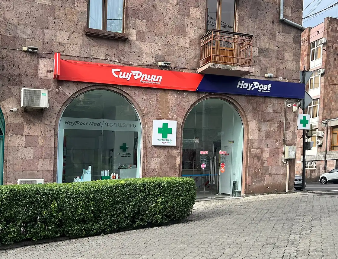 A pharmacy storefront with a green cross sign inside a stone archway in central Yerevan