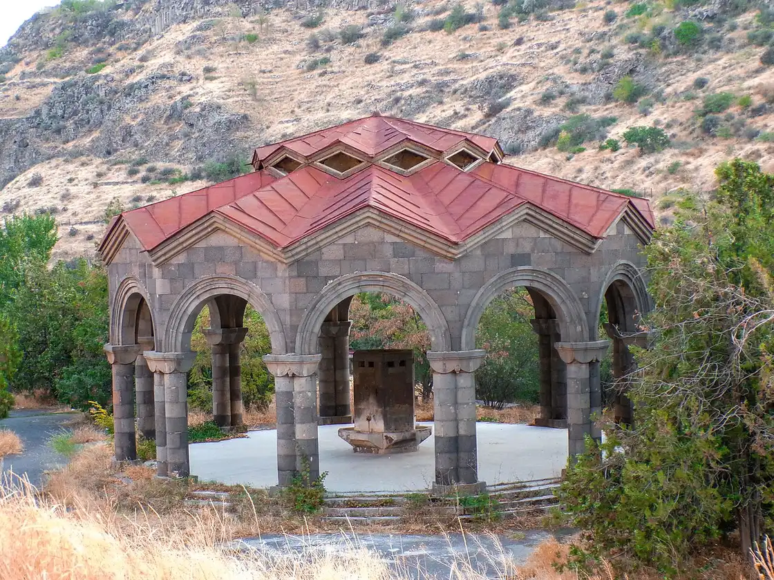 A domed red-roofed stone pavilion over the Arzni mineral water drinking fountain, set against a dry hillside