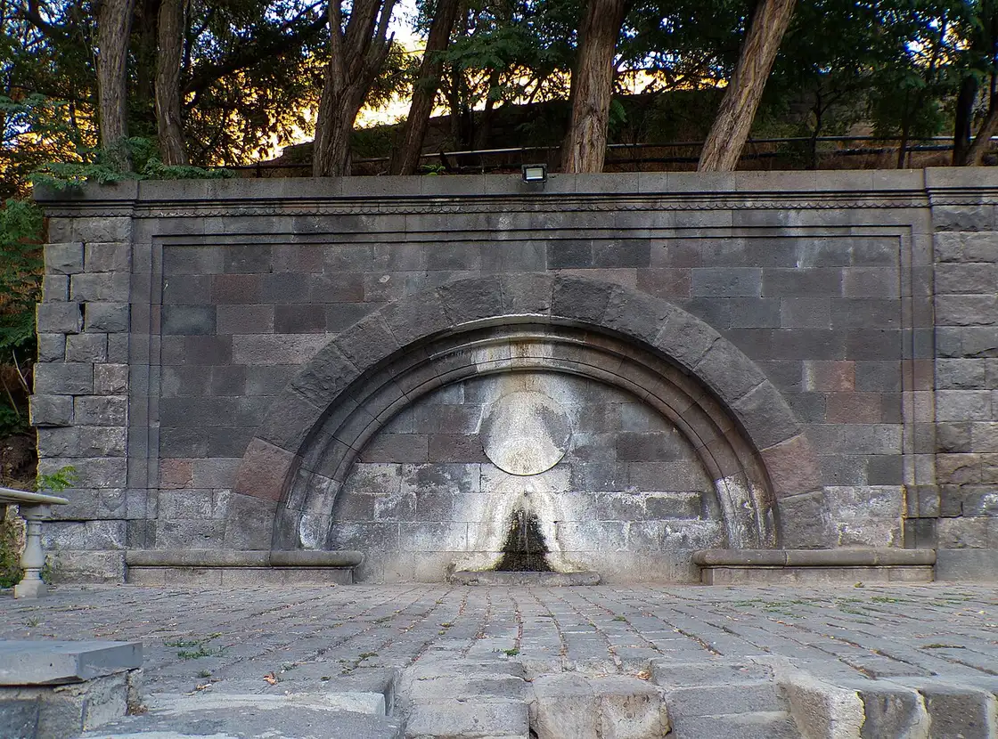 A carved stone archway with a small fountain spout where the Arzni mineral spring is tapped for drinking