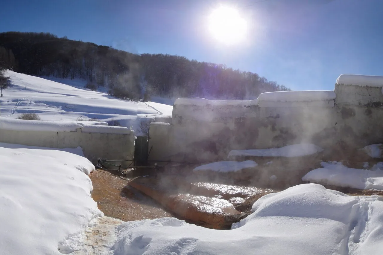 Steam rising off an orange mineral-stained hot spring pool in a snowy Armenian valley, walled with old concrete baths
