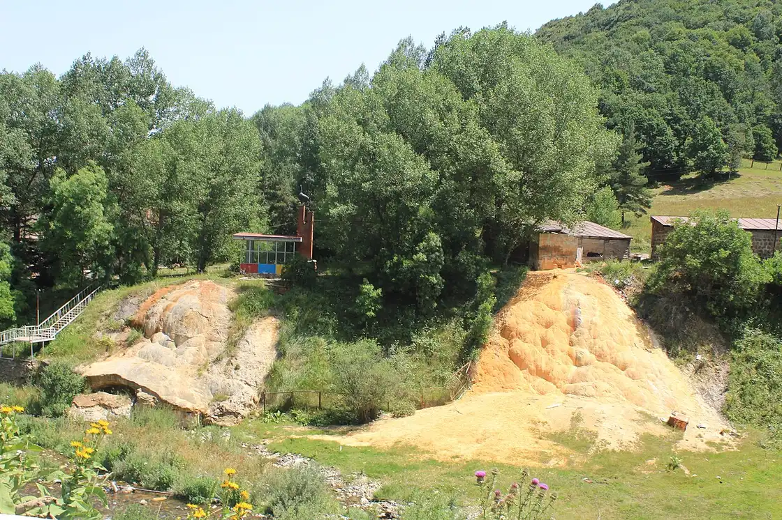 Orange mineral terraces built up by the Hankavan springs beside a small bathhouse and staircase in a forested valley