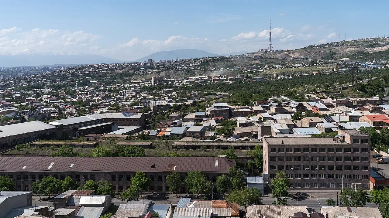 A wide daytime view over Yerevan from the Erebuni hill, the city spreading to the horizon with the snow line of Mount Ararat faint in the distance