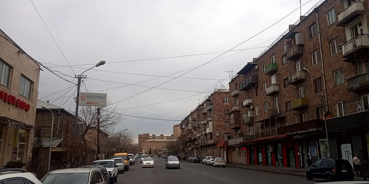An ordinary residential street in Yerevan with parked cars, Soviet-era apartment blocks and a few pedestrians under an overcast sky