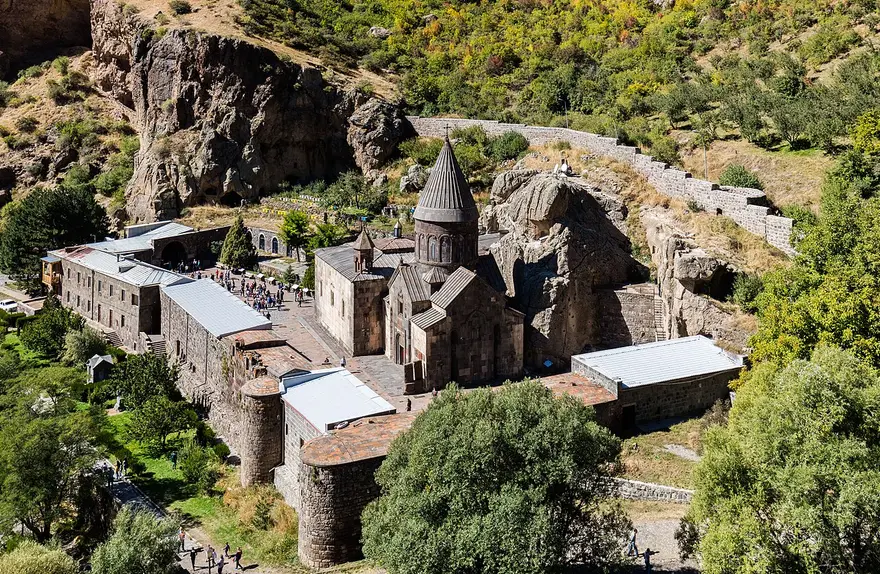 The stone facade of Geghard monastery set against a tall rocky cliff, part of the complex carved directly into the mountain