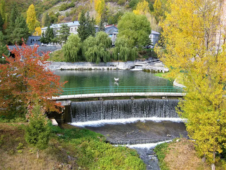 The Arpa river weir and pond in autumn with sanatorium buildings among yellow trees in Jermuk