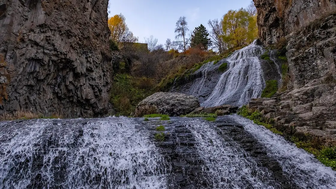 The Jermuk waterfall dropping in a long white ribbon down a cliff into the wooded Arpa gorge on an autumn evening
