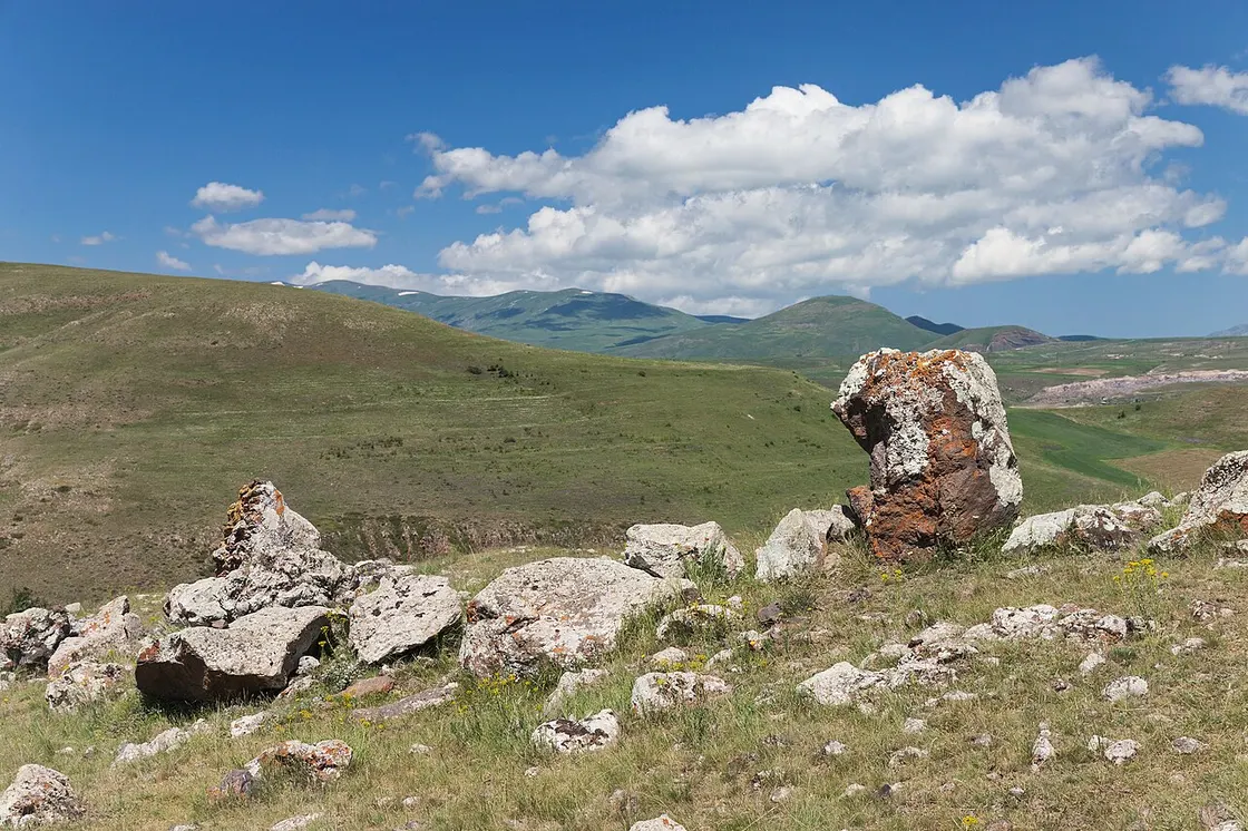 The Karahunj stones on the edge of a high plateau, a rusty monolith among them and green mountain ridges filling the horizon