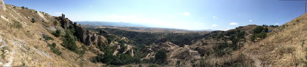 A wide panorama of the Khndzoresk gorge with cave dwellings, cliffs and the bridge in the distance