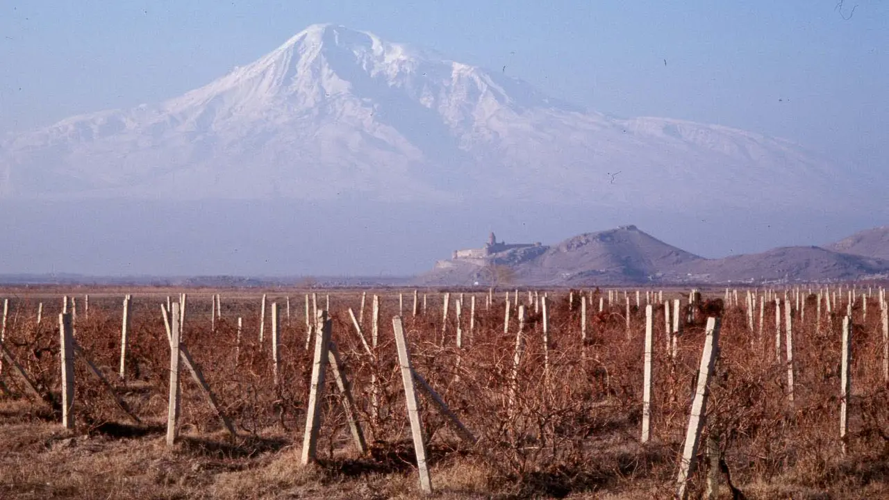 The snow-capped mass of Mount Ararat towering over the small hilltop silhouette of Khor Virap monastery across the vineyards of the Ararat plain