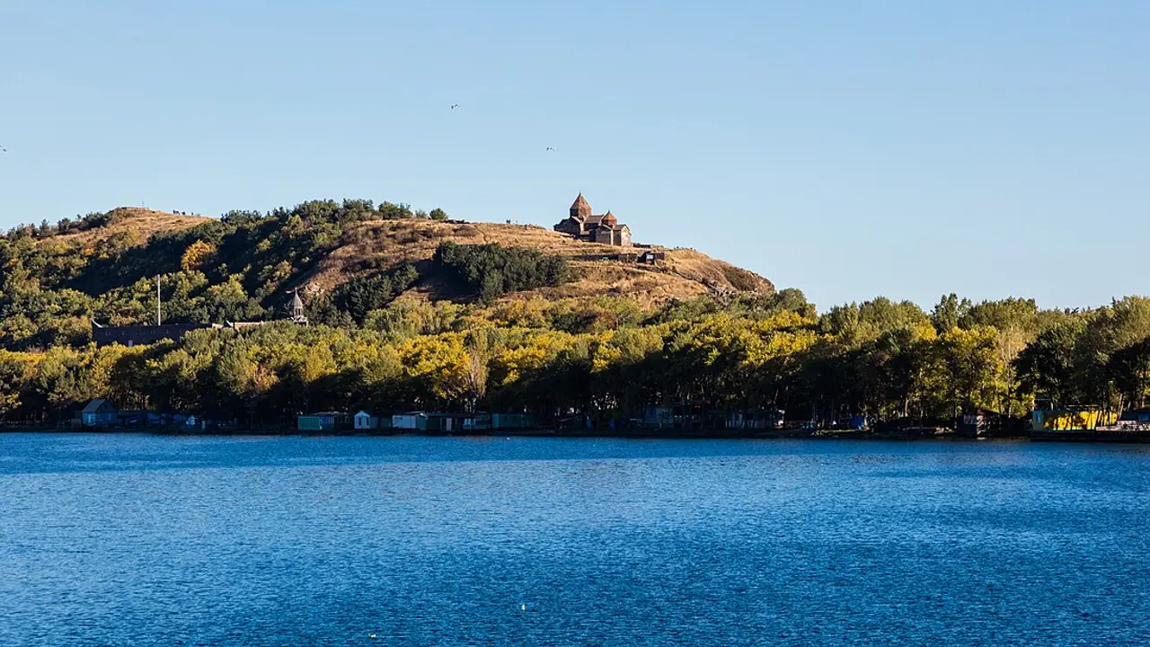The Sevanavank monastery on its wooded hilltop peninsula rising above the deep-blue water of Lake Sevan, with gulls in a clear sky
