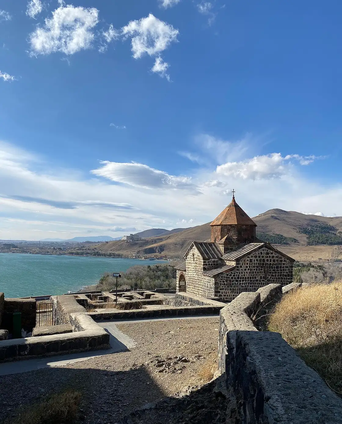 The wide blue expanse of Lake Sevan and its far mountain shore seen from beside a stone church on the Sevanavank peninsula