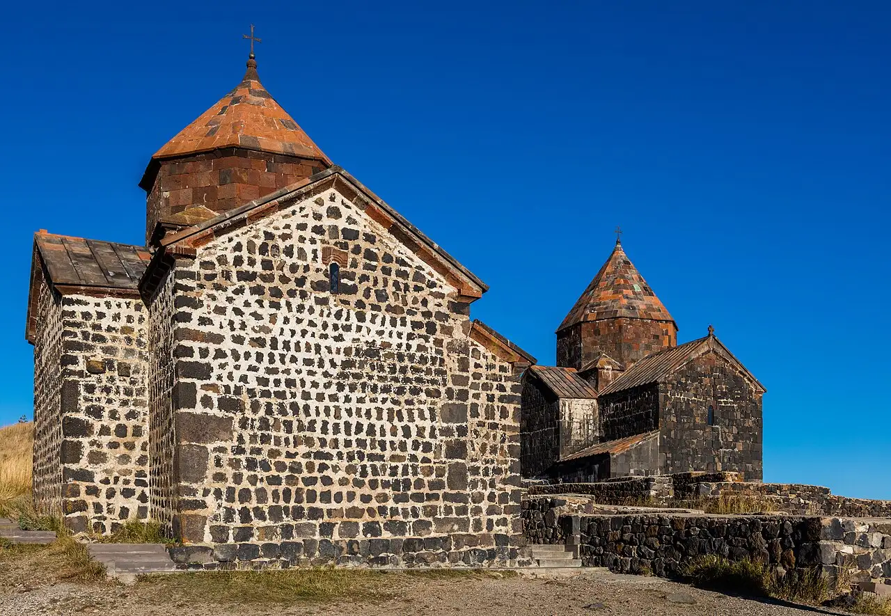 The two surviving churches of Sevanavank, Surb Astvatsatsin and Surb Arakelots, built of dark basalt with red-tuff conical domes against a deep-blue sky