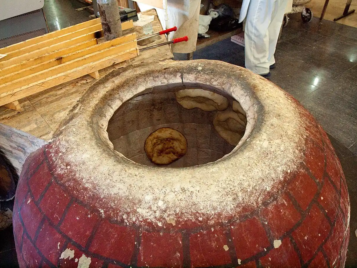Matnakash flatbread baking on the wall of a traditional clay tonir oven