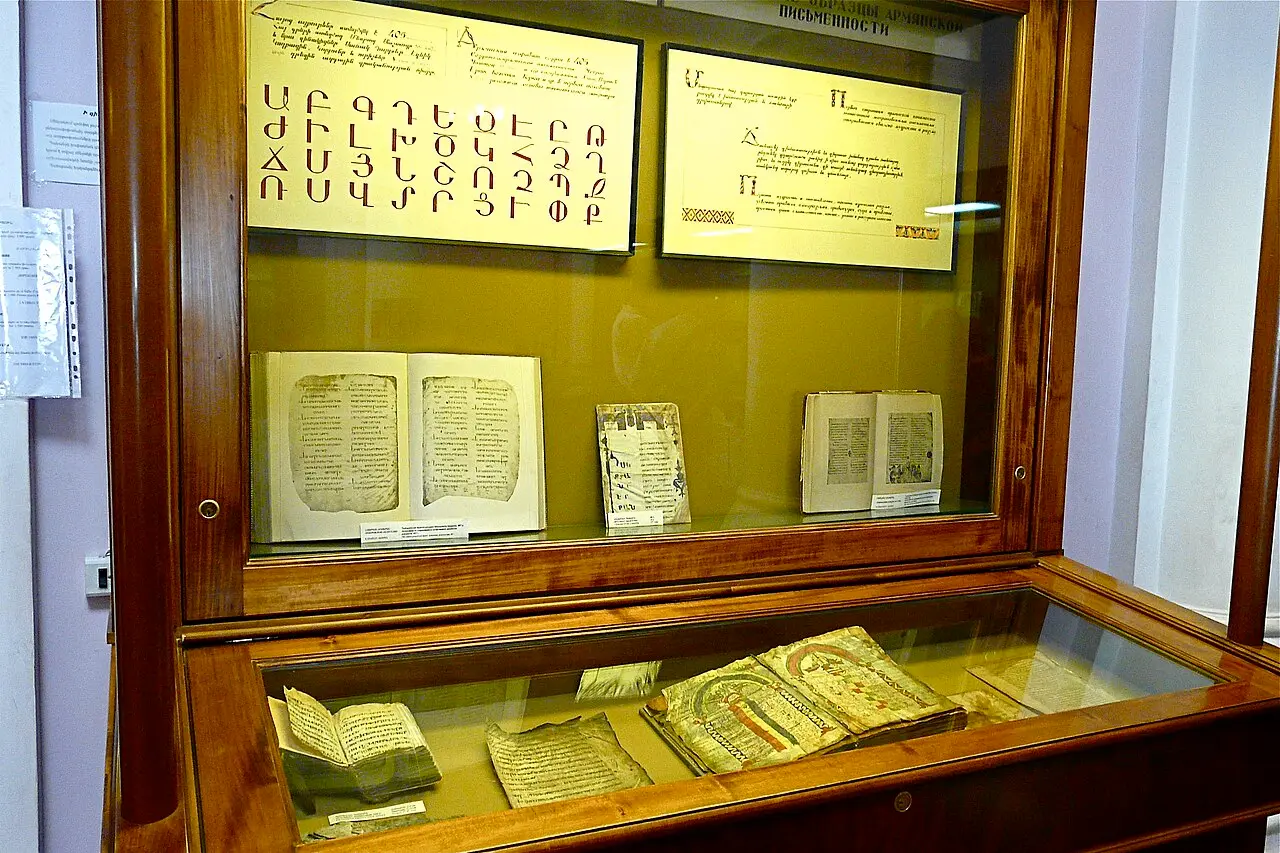 A display case of open illuminated manuscripts and an Armenian alphabet chart inside the Matenadaran museum