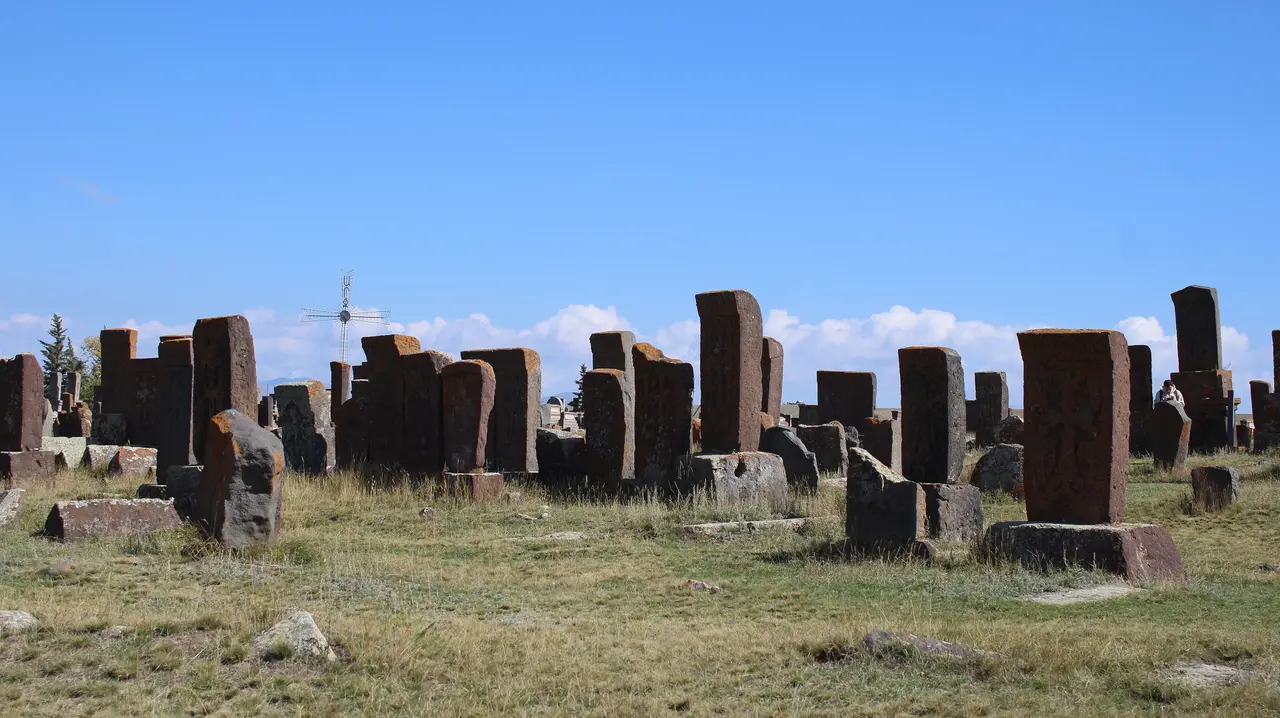 Rows of weathered medieval khachkars standing in a grassy field at Noratus under a deep blue sky