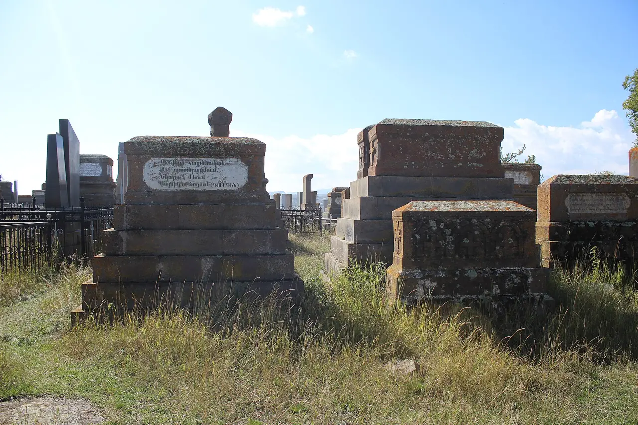 Stepped stone table tombs of the 19th and 20th centuries at Noratus, with an iron railing and modern black granite headstones behind them