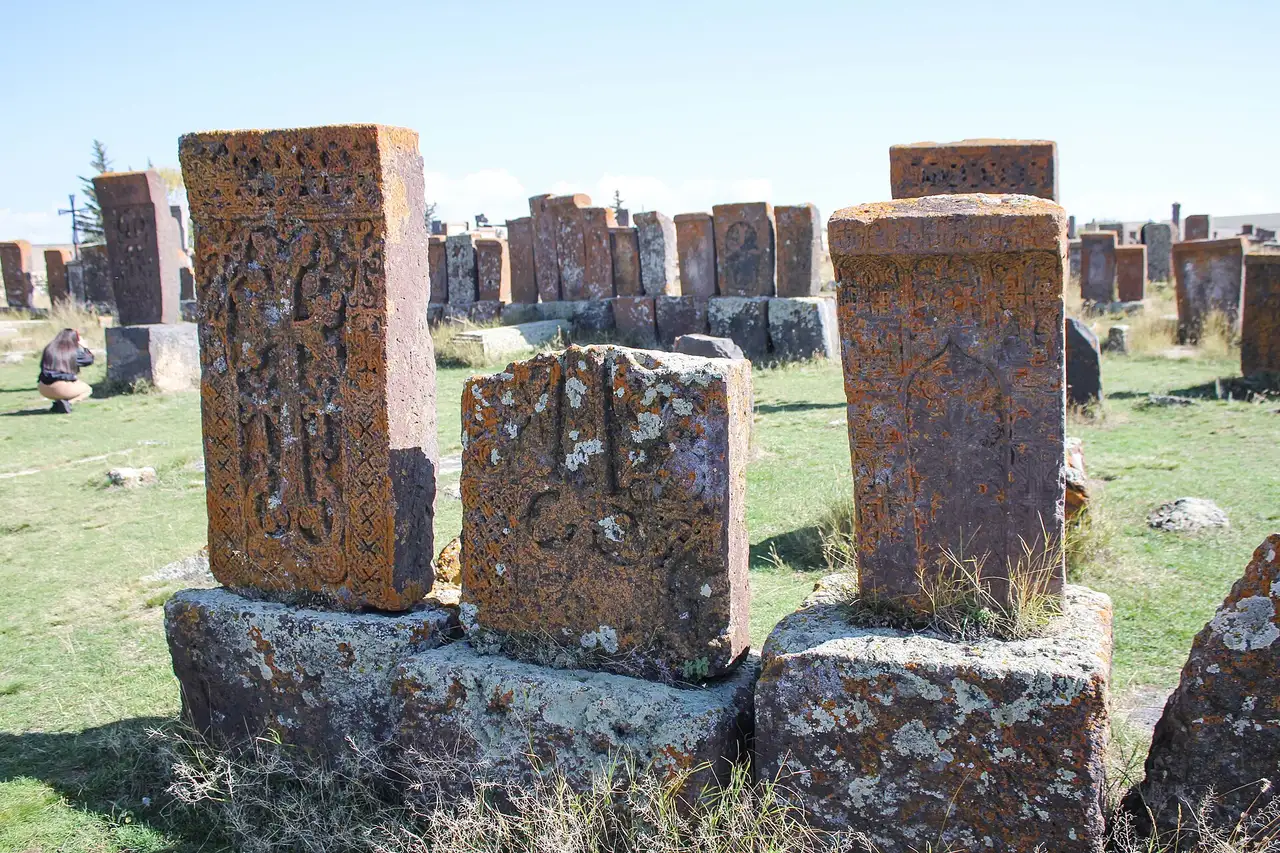 Close-up of three khachkars at Noratus, their carved crosses and interlace half-buried under thick orange and pale green lichen
