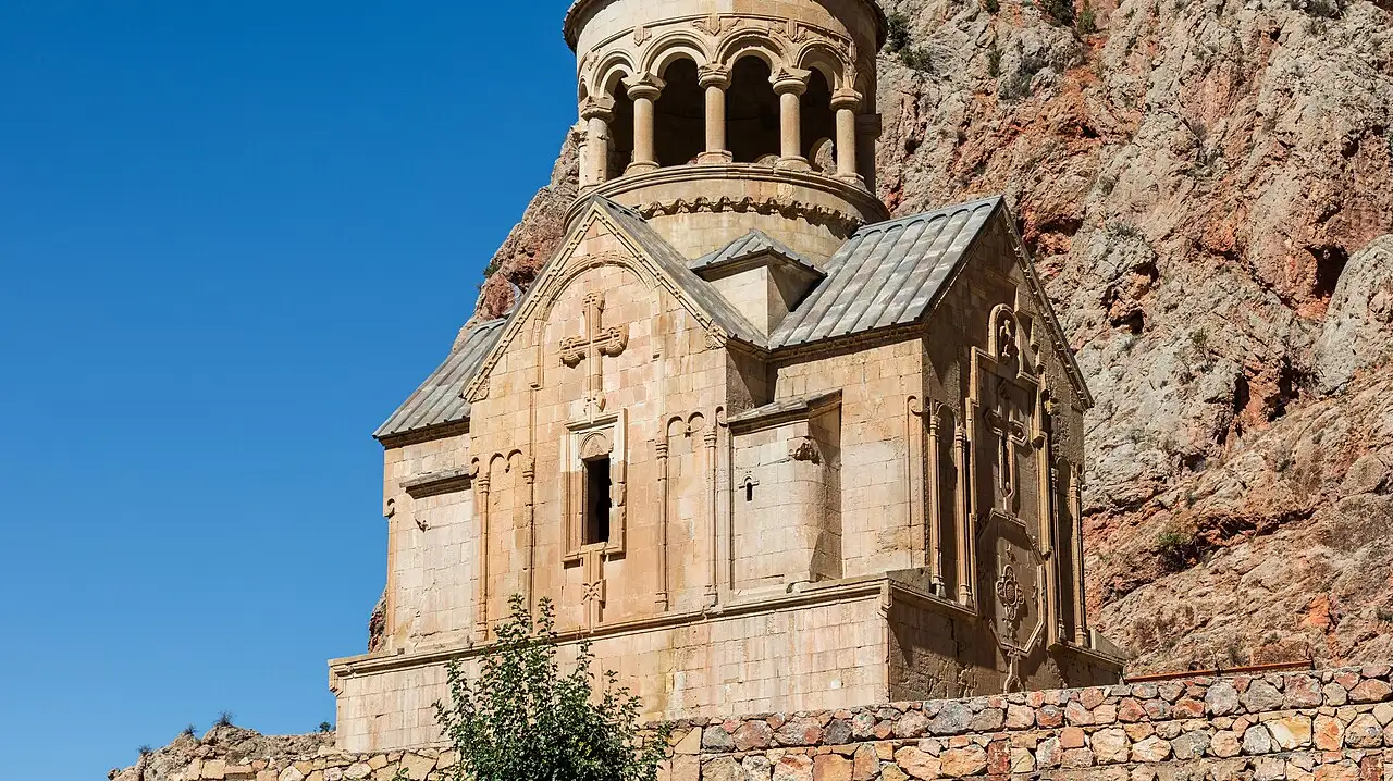 The rotunda belfry and carved gable of the Surb Astvatsatsin church at Noravank glowing against the brick-red cliff of the Amaghu gorge