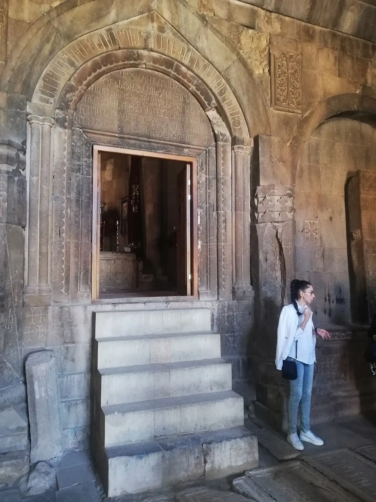 A carved and inscribed stone portal inside Noravank, with an Armenian inscription arching over the doorway and a visitor standing beside it for scale