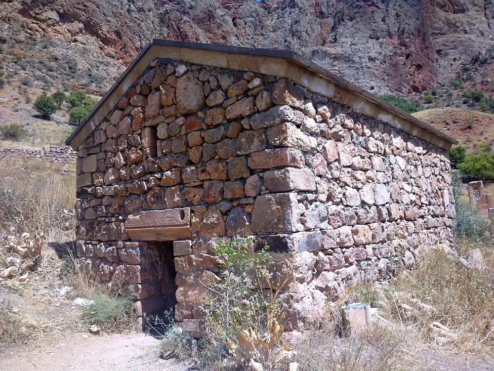 A small dry-stone chapel building in the Noravank complex standing against the deep red rock of the Amaghu canyon