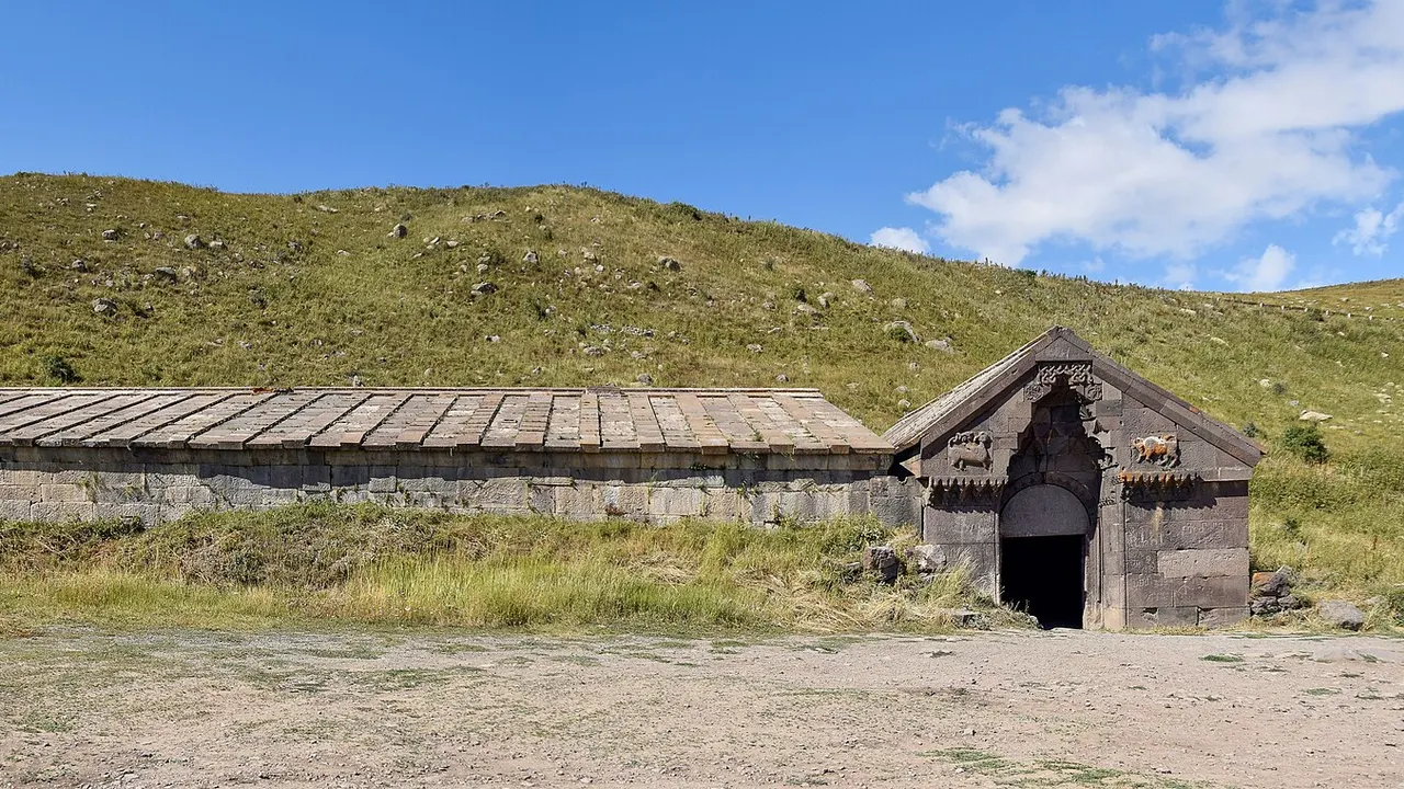 Wide panoramic view of Orbelian caravanserai as a long dark basalt hall on the green highland of the Vardenyats Pass
