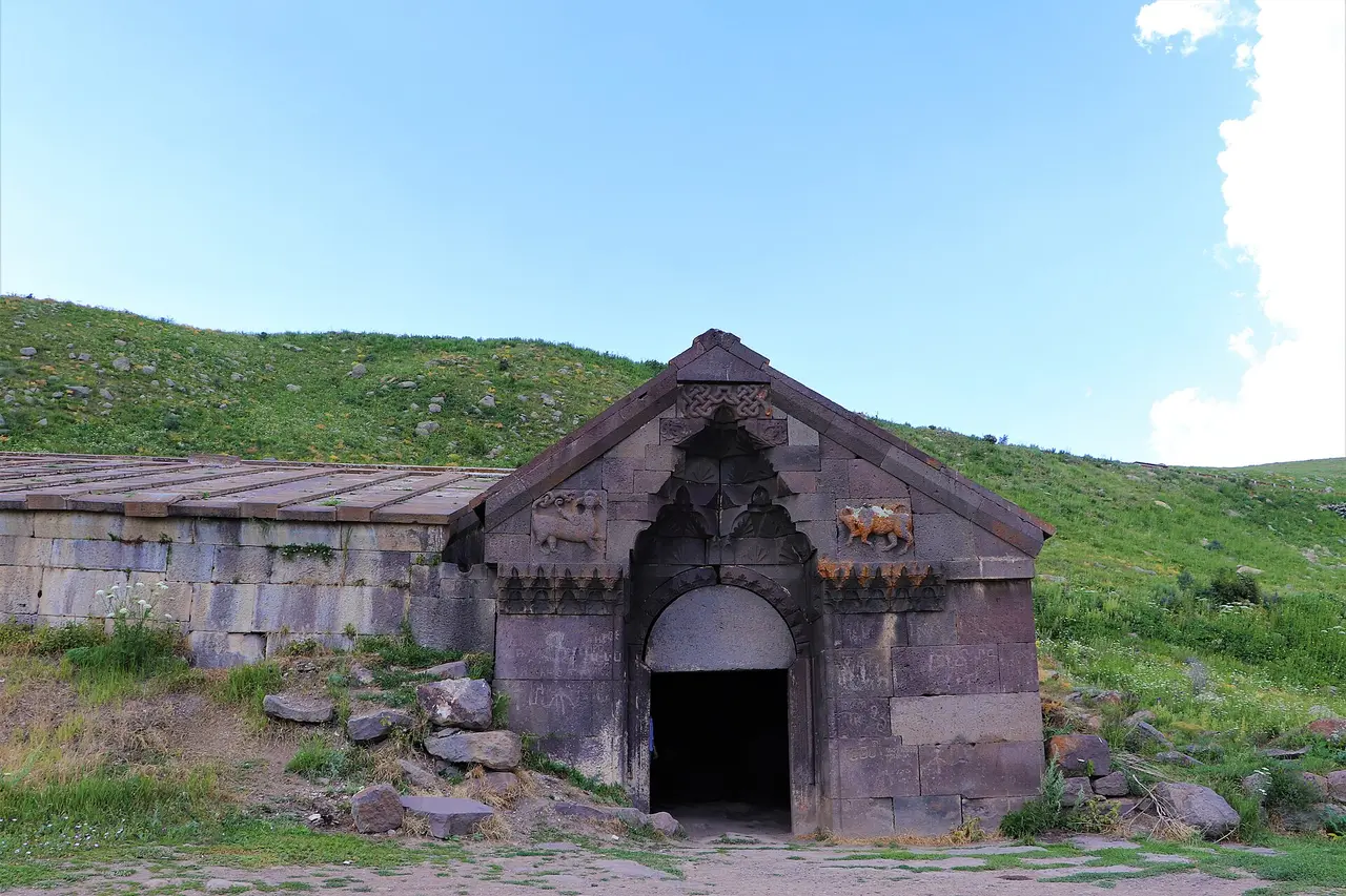 Exterior of Orbelian caravanserai showing the long basalt side wall and gabled roof under a clear highland sky