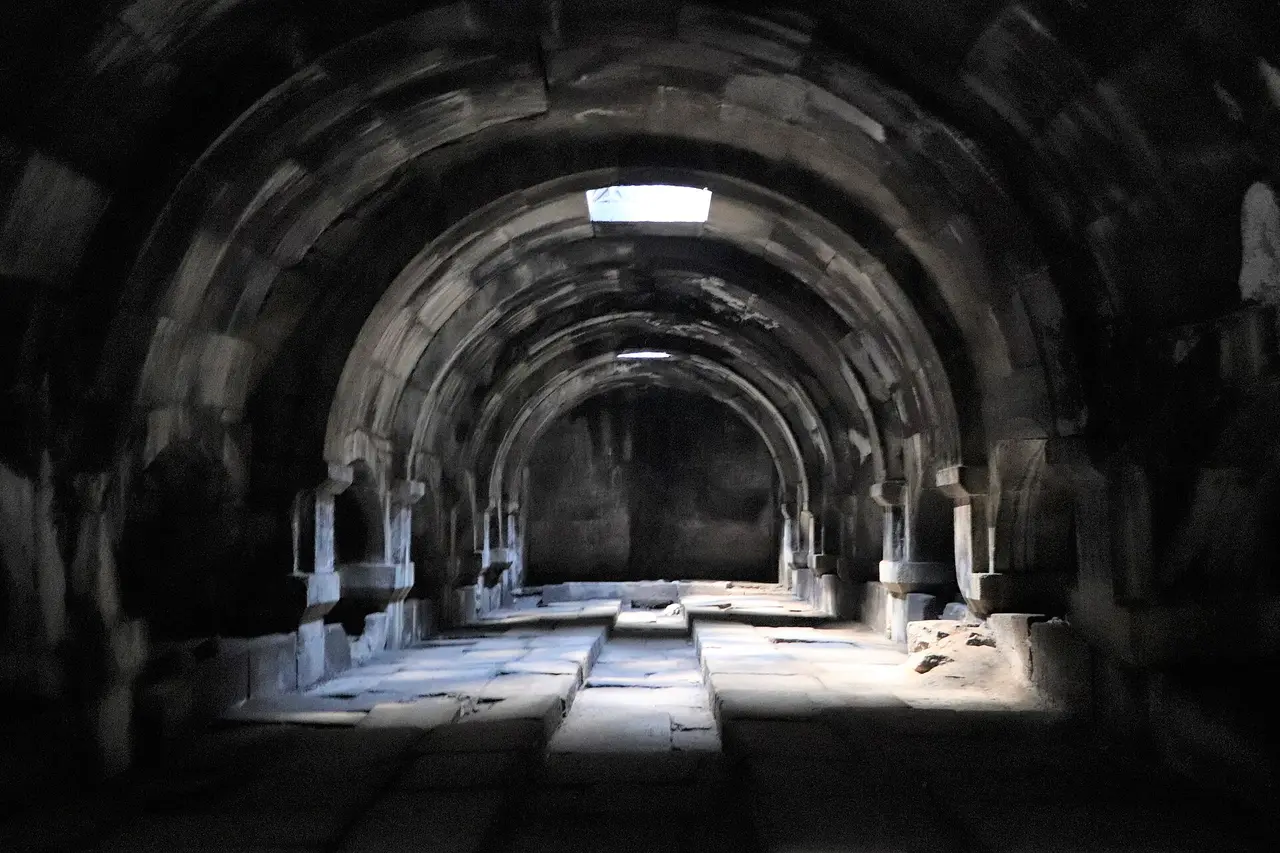 Vaulted basalt interior of Orbelian caravanserai with rows of stone pillars and light falling from roof openings