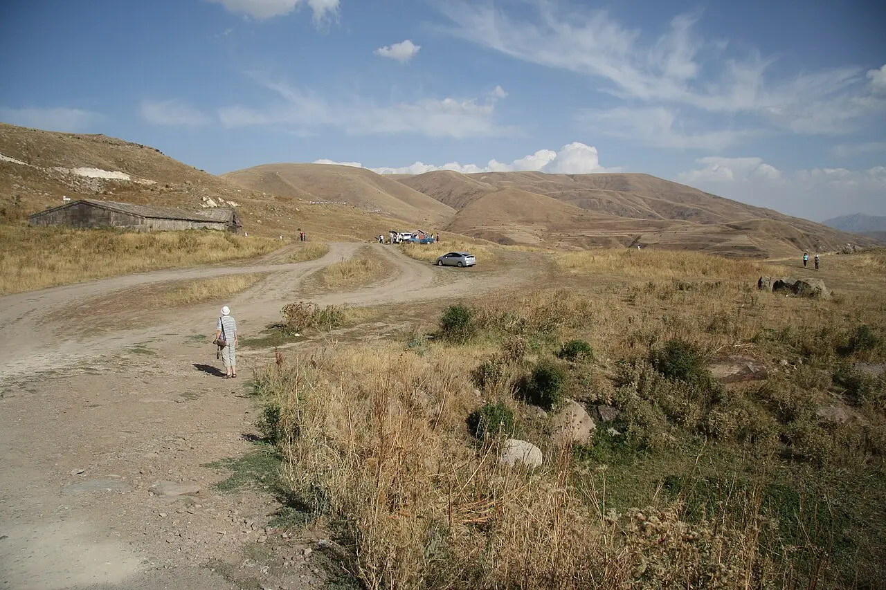 The dark basalt caravanserai sitting alone in open highland pasture on the Selim Pass with bare ridges behind