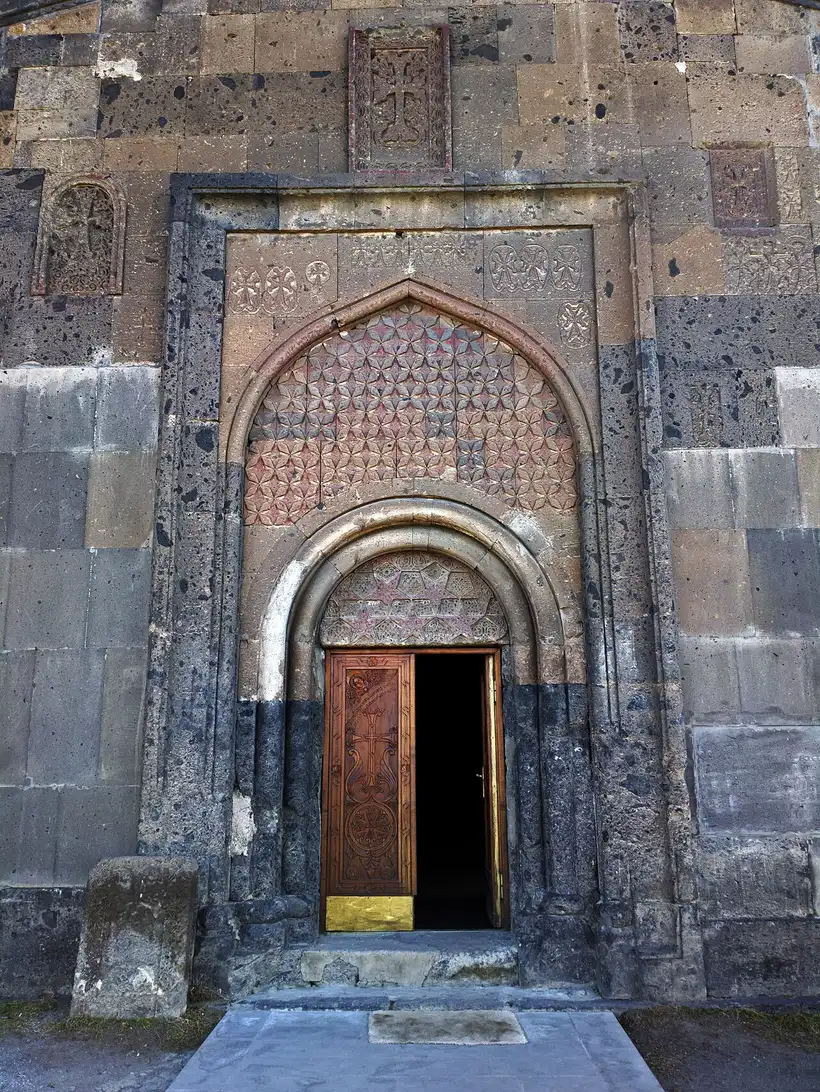 The deeply carved stone portal of the gavit at Saghmosavank, with an interlaced star pattern in the tympanum and khachkars set into the wall above