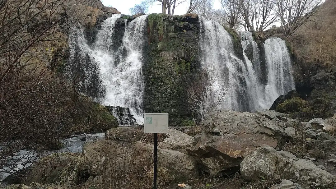 The Shaki waterfall running strongly in December, with an information board on a post in front of it and bare trees along the ledge