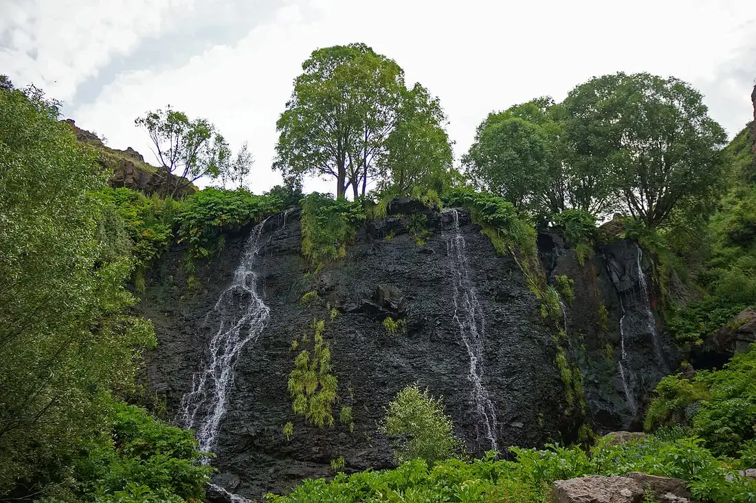 The Shaki ledge with only thin scattered threads of water running down the dark mossy rock and trees along the top