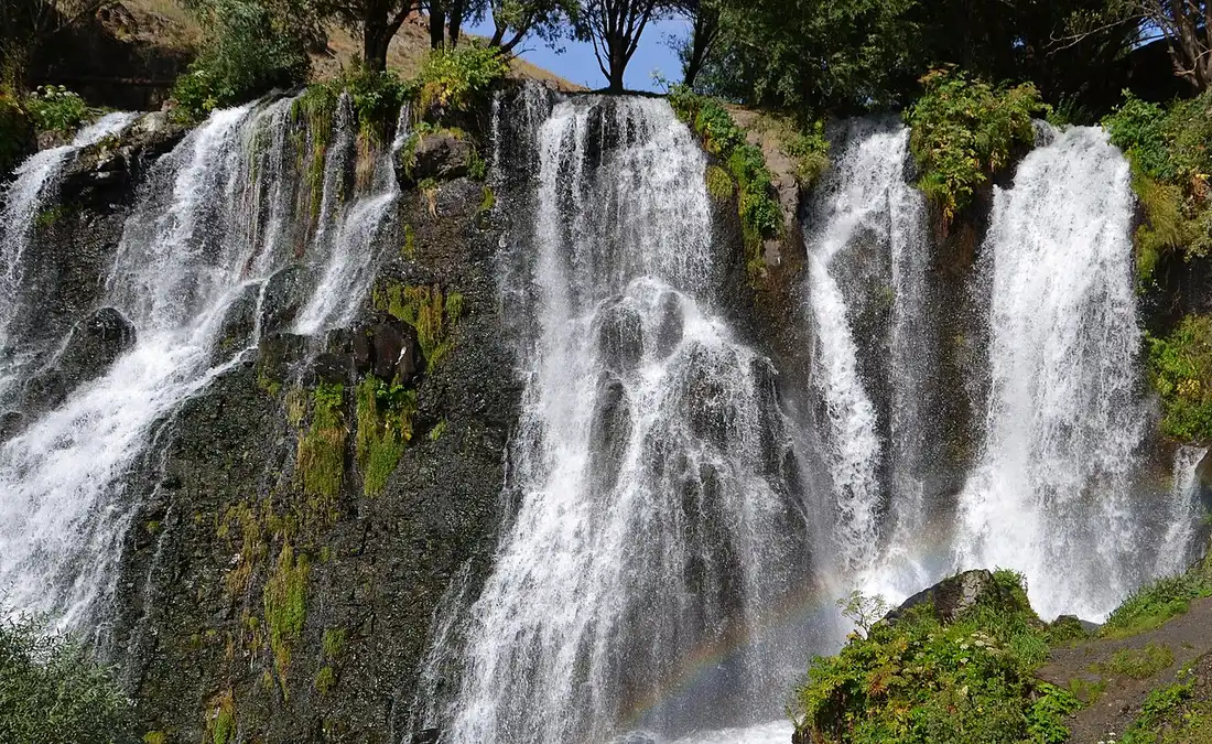 Close view of the Shaki waterfall with a faint rainbow forming in the spray at the foot of the mossy basalt cliff