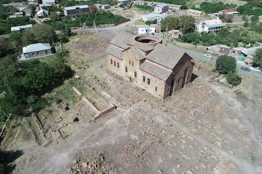 The large dome-less basilica of Aruch cathedral among excavated foundations at the foot of Mount Aragats