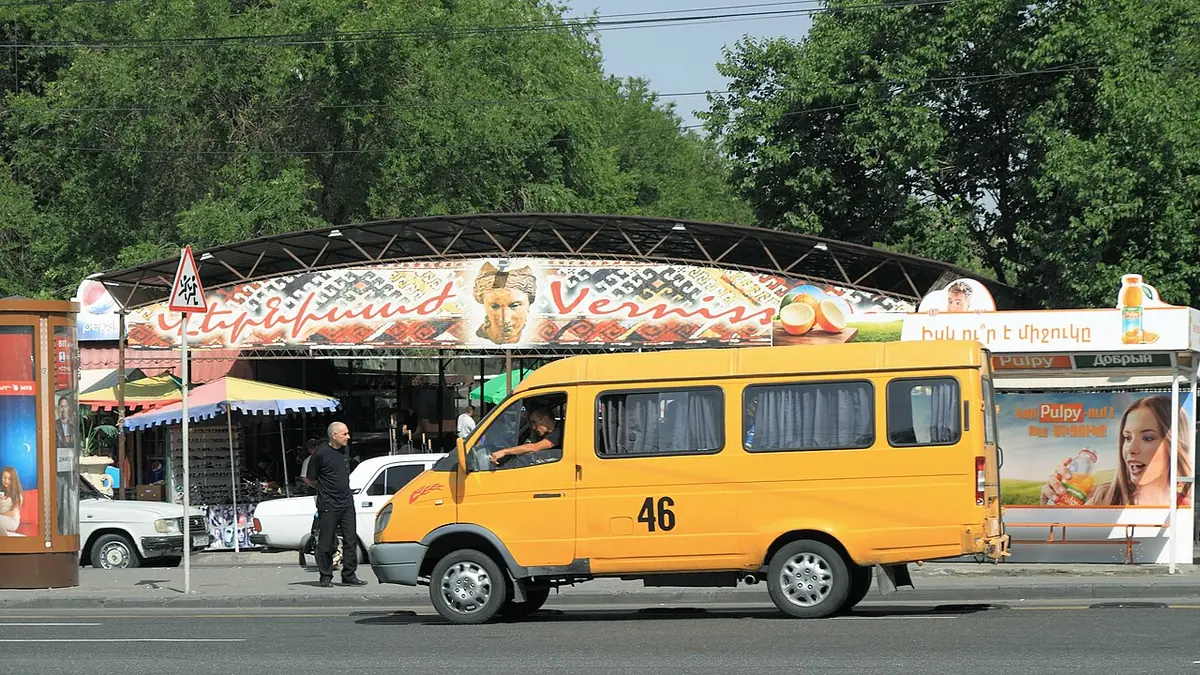 A white marshrutka minibus parked on a central Yerevan street among other traffic