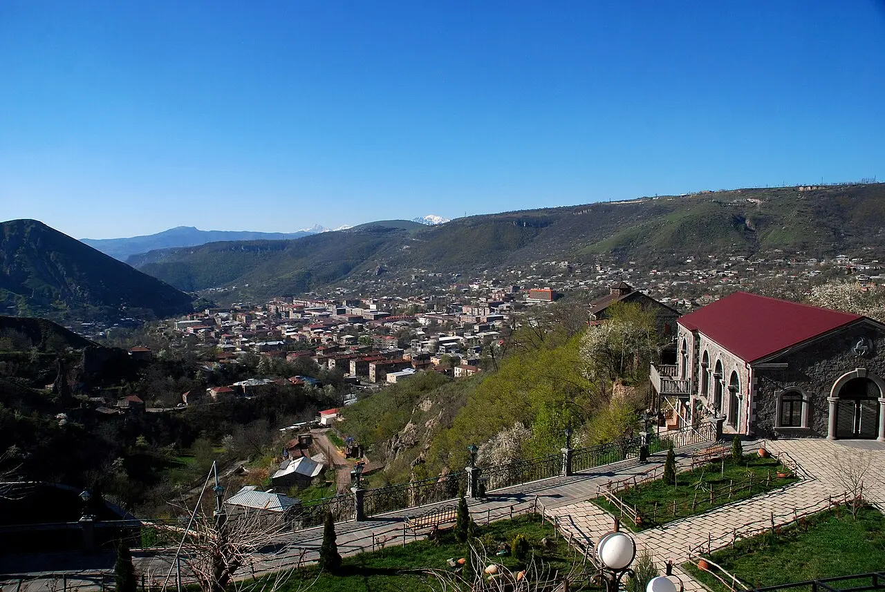 The town of Goris spread across a green valley in Syunik, ringed by wooded hills, seen from an eastern slope