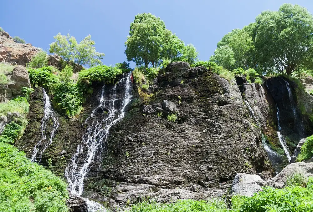 The Shaki waterfall spilling in thin white streams down a broad dark basalt ledge topped with green trees near Sisian