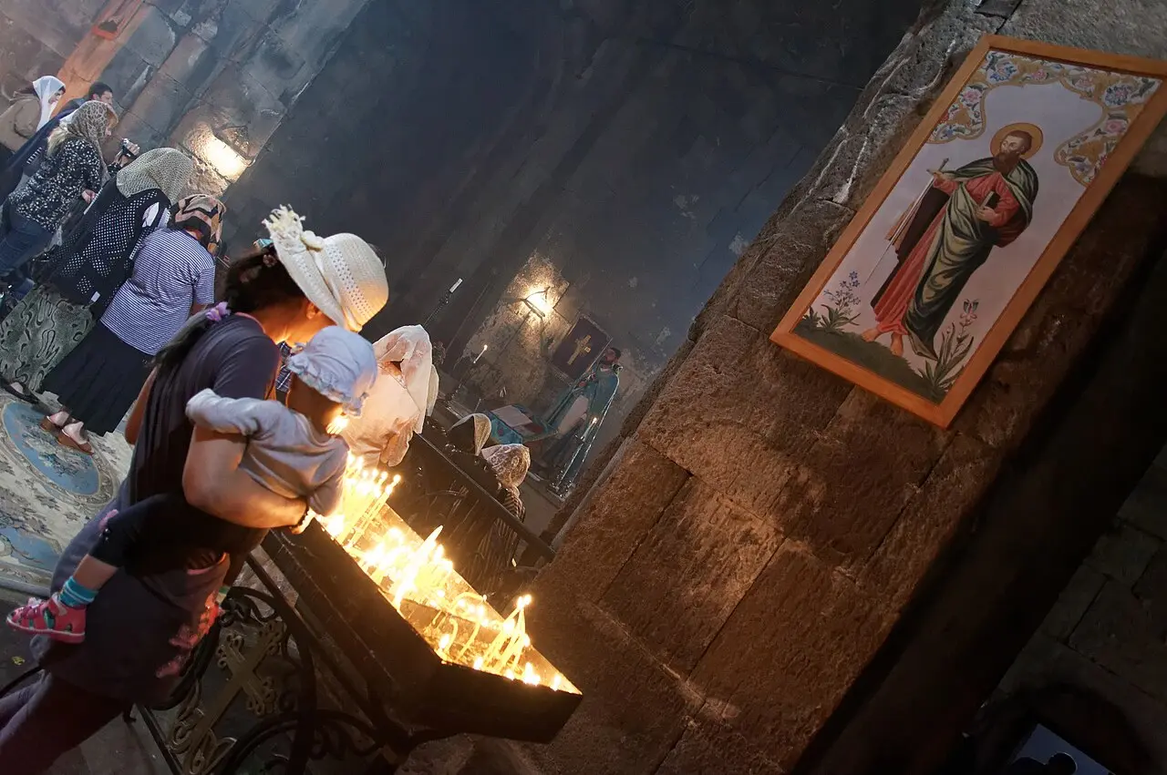 Rows of thin votive candles burning in the dim stone interior of a church at Tatev monastery