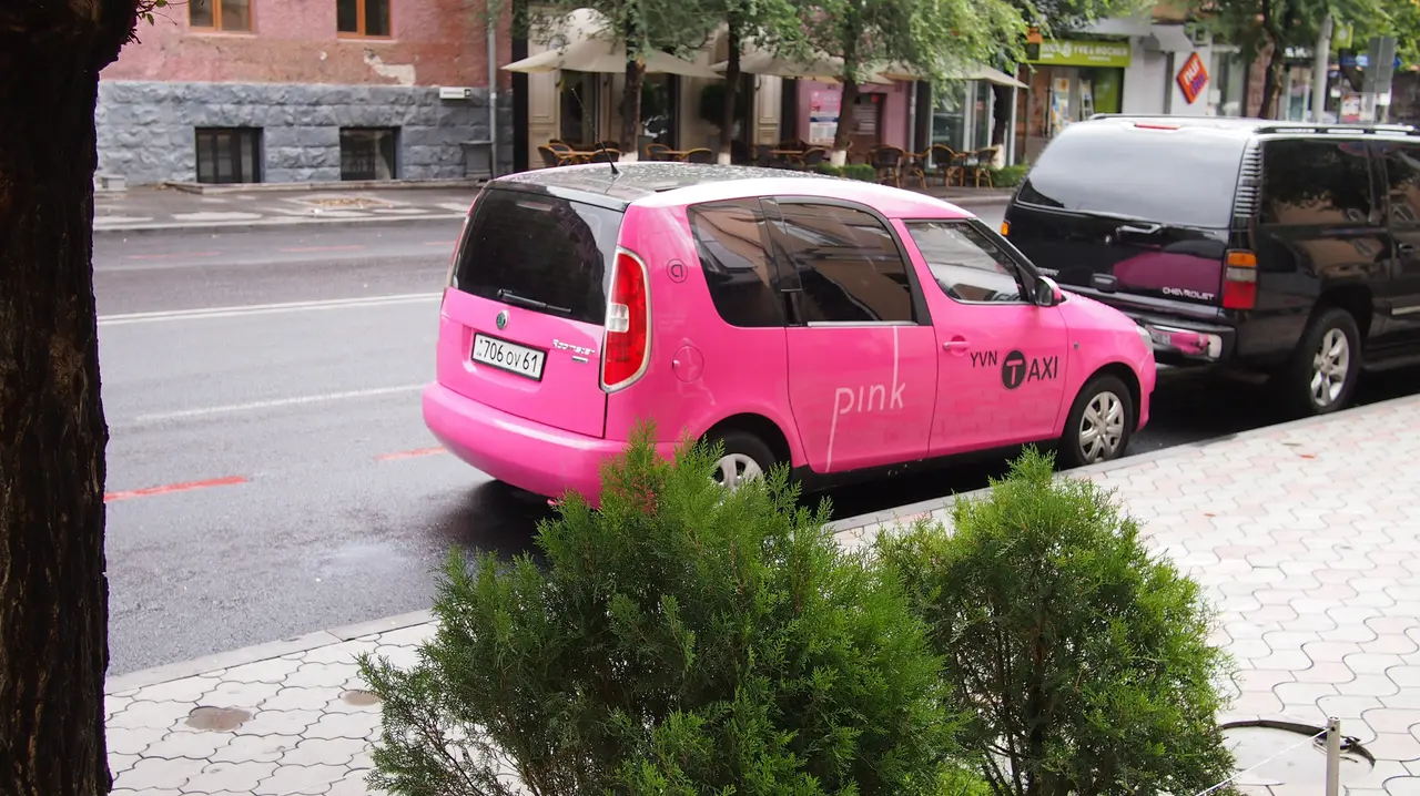 A bright pink Pink Taxi car parked on a wet street in central Yerevan, Armenia