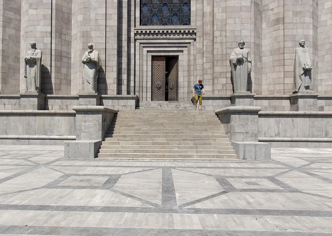 The grey basalt facade and entrance stairway of the Matenadaran manuscript museum in Yerevan, flanked by statues of Armenian scholars