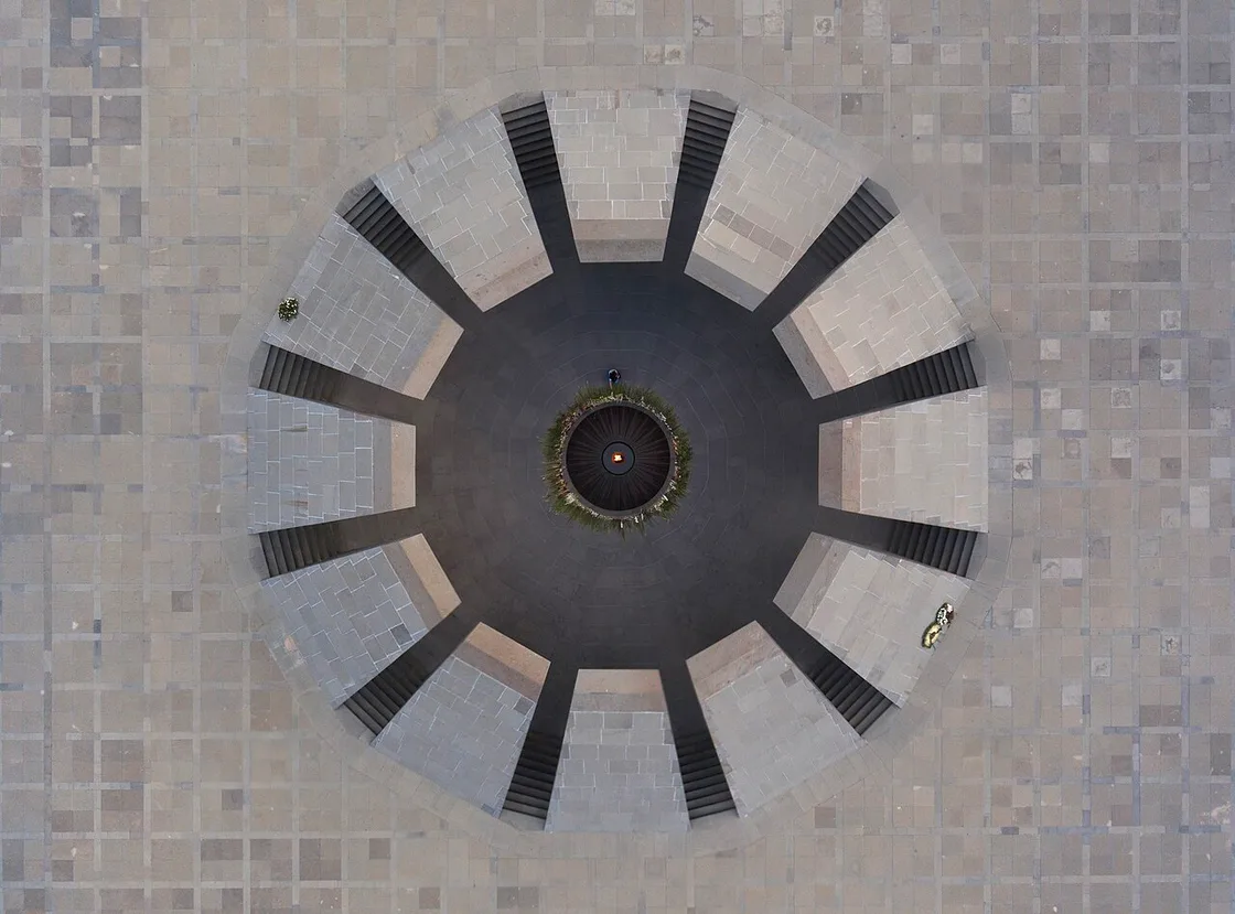 Aerial view of the twelve leaning stone pylons circling the eternal flame at the Tsitsernakaberd Armenian Genocide Memorial, with a visitor laying flowers