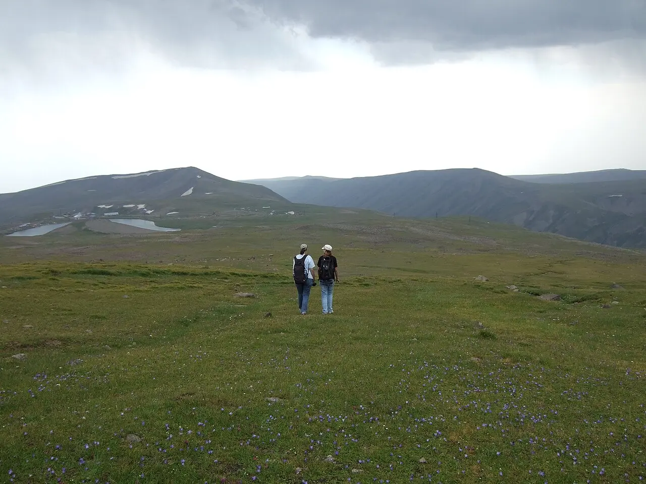 Two hikers standing on the high grassy alpine plateau of Mount Aragats with lakes and peaks behind them