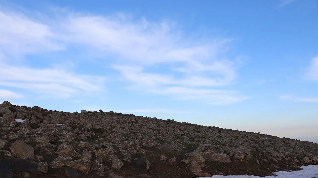 The bare rocky high slopes of Mount Aragats under a wide blue sky with a patch of snow