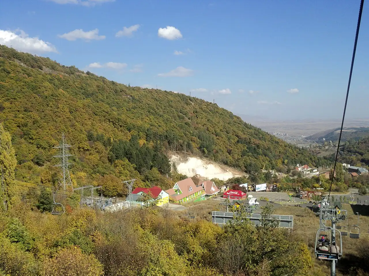 The view from a Tsaghkadzor chairlift over forested autumn slopes down to the resort buildings and valley