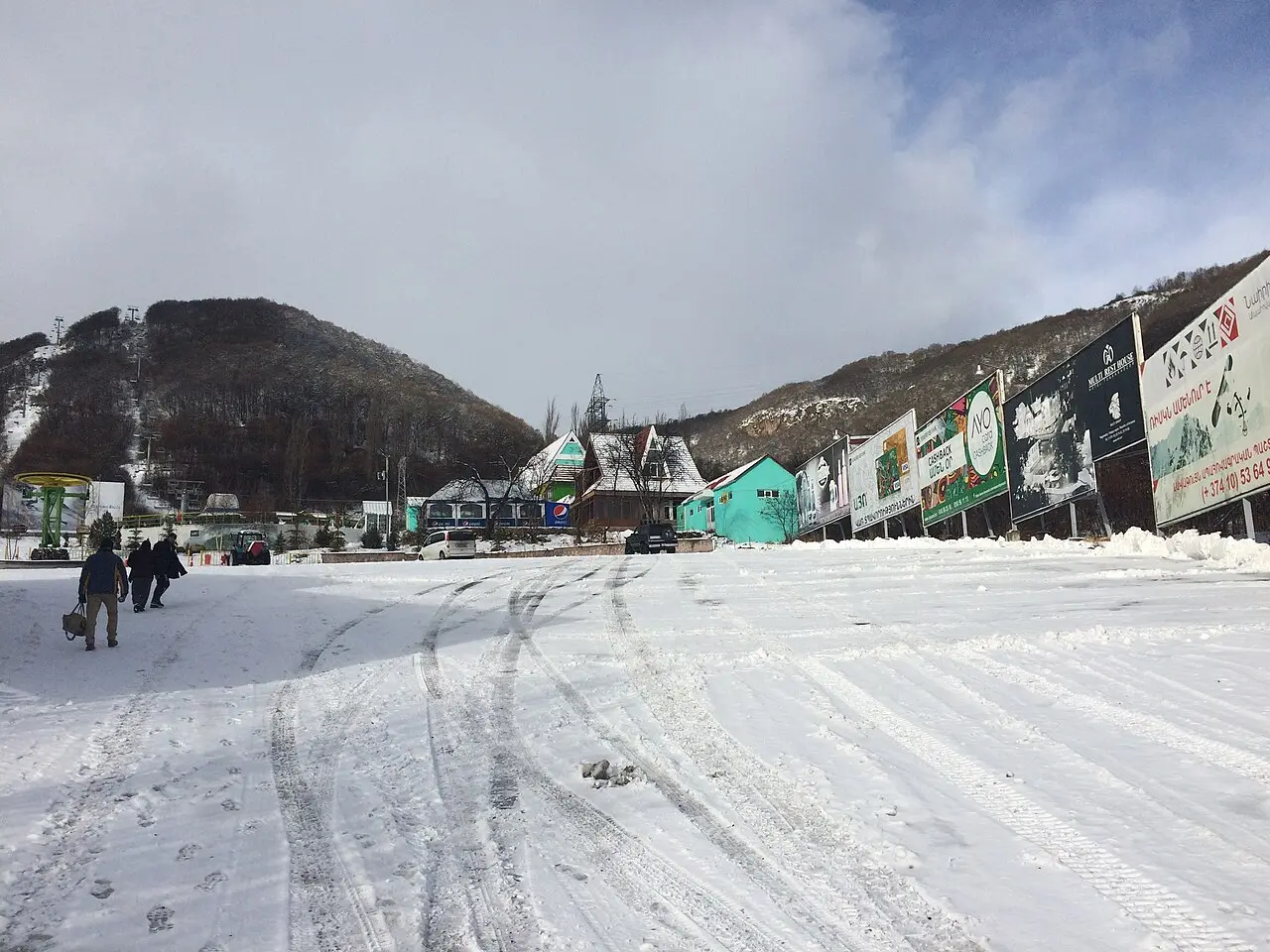 The snowy base area of the Tsaghkadzor ropeway in early December with billboards and people walking