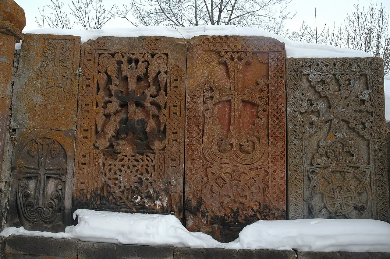 A row of intricately carved khachkars (cross-stones) in different colours of tufa at Kecharis, snow on top