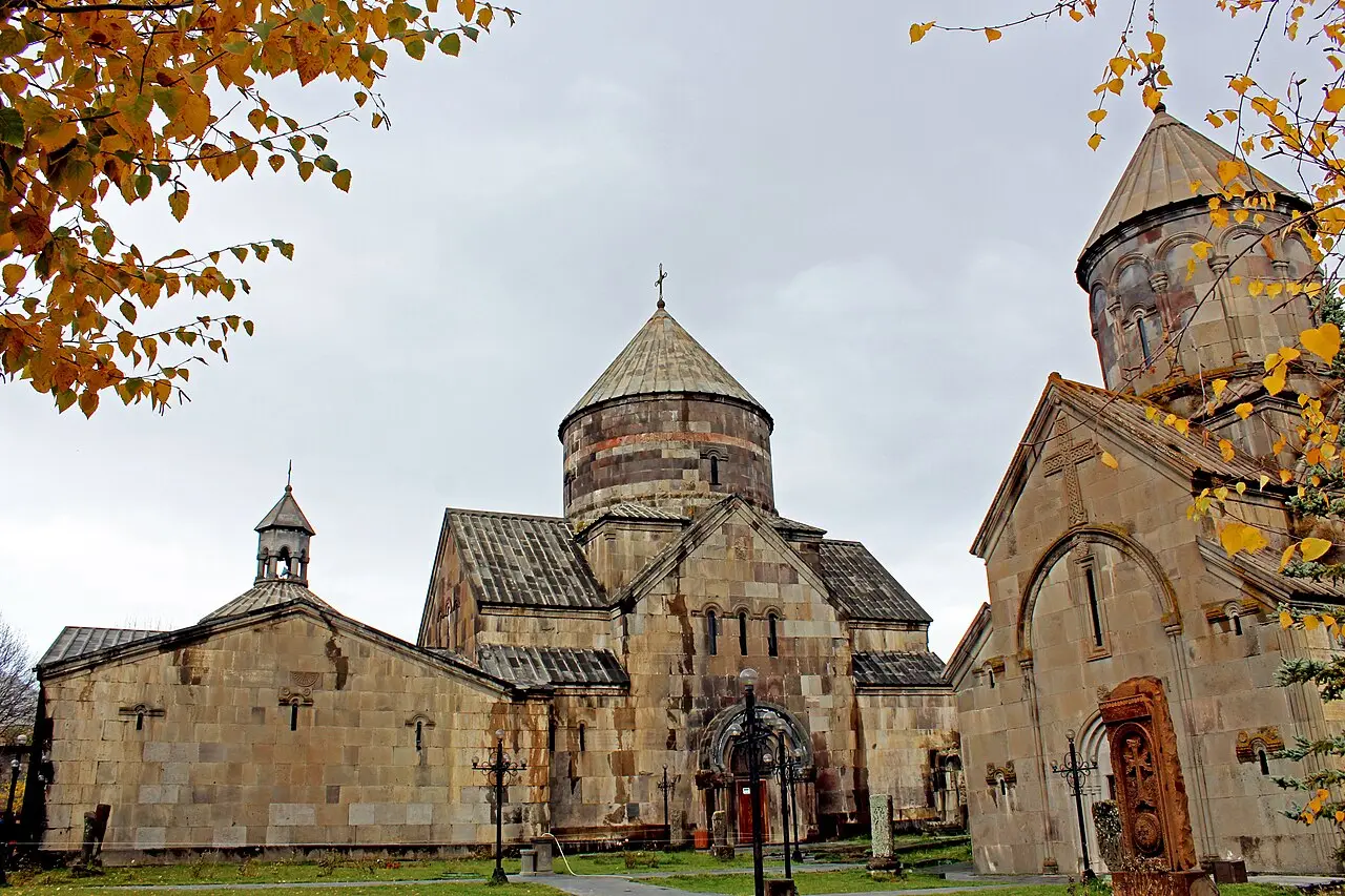 The grey stone churches and conical domes of Kecharis Monastery framed by golden autumn birch leaves