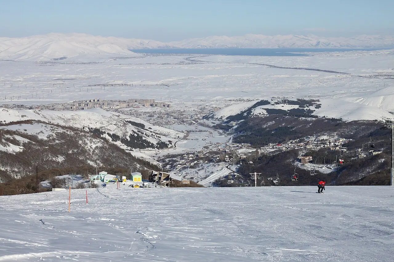 A skier on a groomed piste high above Tsaghkadzor with the town below and Lake Sevan on the horizon