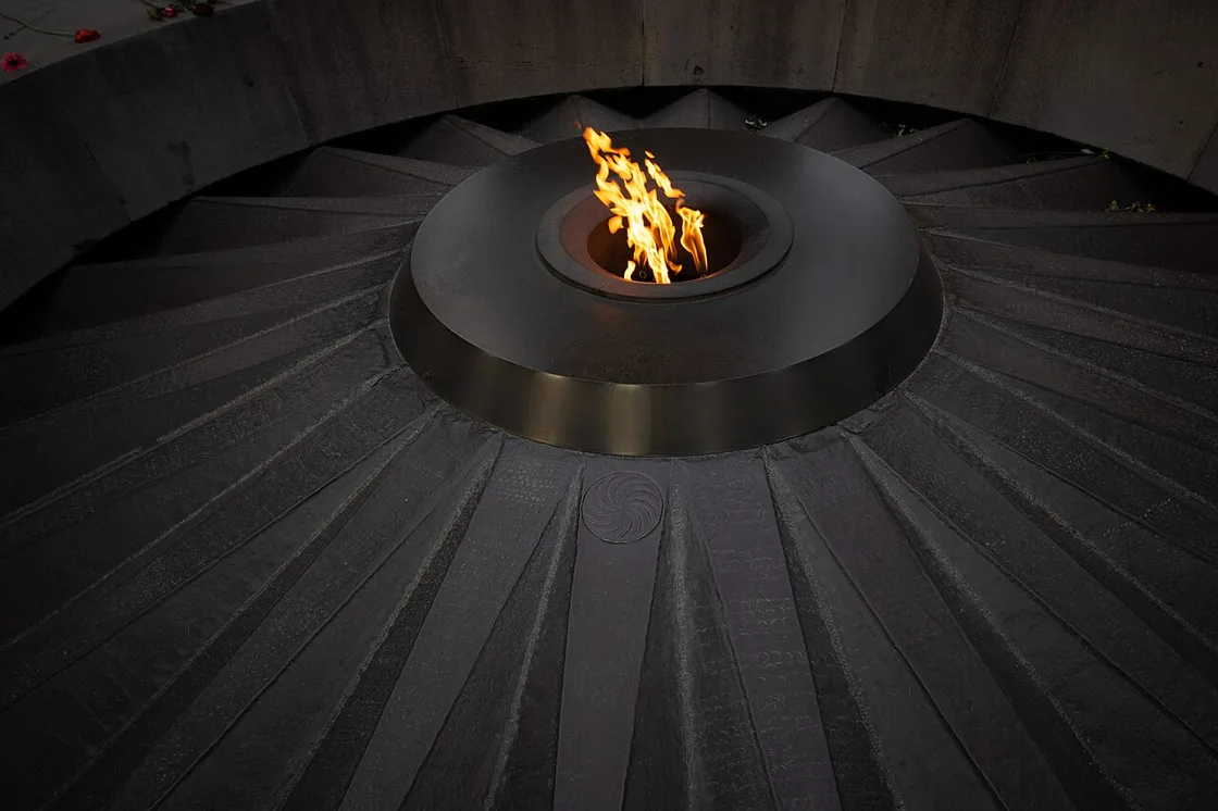 The eternal flame burning at the centre of the sunken circle of twelve slabs at Tsitsernakaberd, with a few red flowers laid at the rim