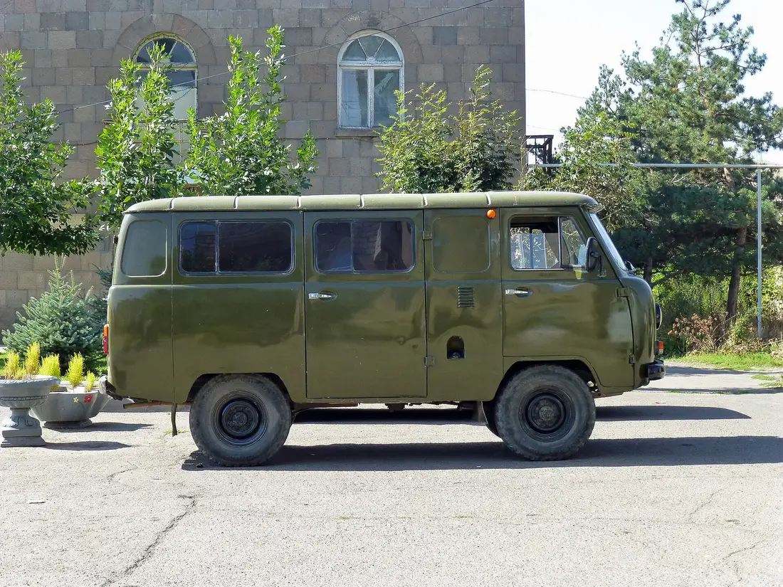 An olive-green UAZ-452 van parked on asphalt in front of a stone building in Sisian, the kind of high-clearance 4x4 used for the Ughtasar track