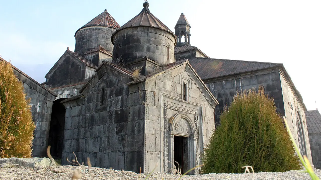 The dark stone churches and conical domes of Haghpat monastery seen from below against a pale sky